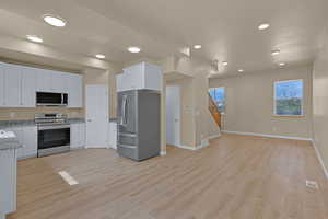Kitchen with light wood-type flooring, appliances with stainless steel finishes, light stone counters, and white cabinets