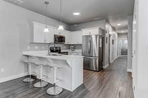 Kitchen with dark wood-type flooring, light countertops, appliances with stainless steel finishes, and a peninsula