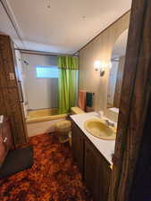 Bathroom featuring shower / bath combination with curtain, toilet, vanity, and wooden walls