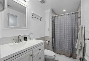 Bathroom featuring toilet, curtained shower, vanity, and visible vents