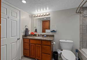 Bathroom with toilet, tiled shower, vanity, and a textured ceiling