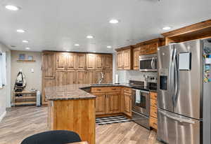 Kitchen featuring light wood-style flooring, recessed lighting, appliances with stainless steel finishes, a sink, and brown cabinets
