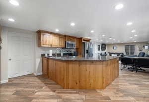 Kitchen with dark countertops, appliances with stainless steel finishes, a peninsula, recessed lighting, and light wood-style flooring