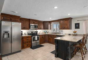 Kitchen with light tile patterned floors, a breakfast bar area, appliances with stainless steel finishes, and a peninsula