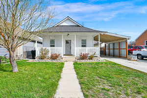 View of front of home featuring a front yard, a porch, an attached carport, and roof with shingles