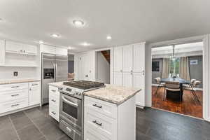 Kitchen with white cabinets, a kitchen island, appliances with stainless steel finishes, and open shelves