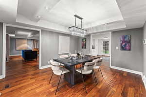 Dining area featuring a chandelier, a raised ceiling, baseboards, visible vents, and dark wood-type flooring
