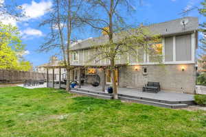 Back of house with fence, a wooden deck, a patio, brick siding, and a yard