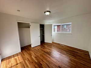 Unfurnished bedroom featuring brick wall, multiple closets, and wood finished floors