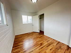 Unfurnished bedroom featuring brick wall, a closet, and wood finished floors