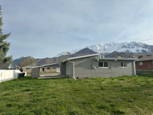 Back of house with a mountain view, fence, and a lawn