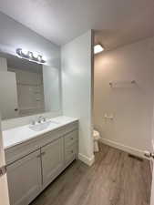 Full bath with a textured ceiling, vanity, visible vents, toilet, and wood finished floors