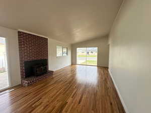 Unfurnished living room featuring wood finished floors, a wood stove, baseboards, and lofted ceiling