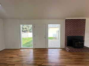 Unfurnished living room featuring a healthy amount of sunlight, a wood stove, and wood finished floors