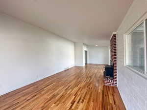 Unfurnished living room with brick wall, wood finished floors, a fireplace, and visible vents