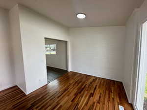 Empty room with brick wall, dark wood finished floors, and visible vents