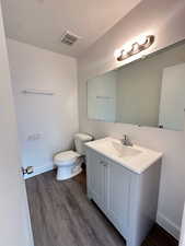 Bathroom featuring vanity, visible vents, toilet, wood finished floors, and baseboards