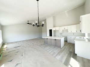 Kitchen with a kitchen island, white cabinetry, high vaulted ceiling, a chandelier, and a kitchen breakfast bar