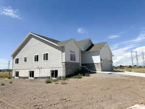 View of side of home with board and batten siding, concrete driveway, roof with shingles, an attached garage, and stone siding