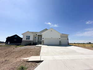 View of front of property with board and batten siding, a garage, stone siding, and concrete driveway