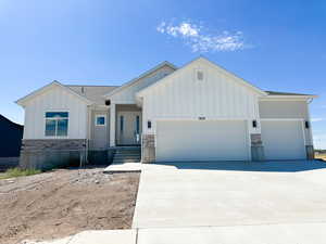 View of front of home featuring board and batten siding, an attached garage, concrete driveway, and stone siding