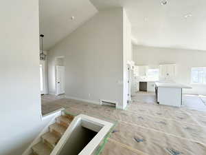 Unfurnished living room with high vaulted ceiling and stairway
