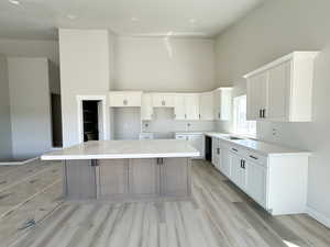 Kitchen featuring a towering ceiling, a kitchen island, white cabinets, light stone counters, and light wood finished floors
