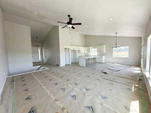 Unfurnished living room featuring high vaulted ceiling, a chandelier, and a ceiling fan