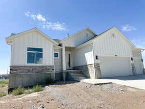 View of front of property featuring stone siding, driveway, board and batten siding, and a garage