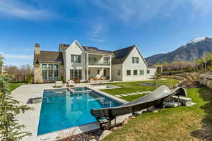 Rear view of property featuring a patio area, a balcony, a lawn, stone siding, and solar panels