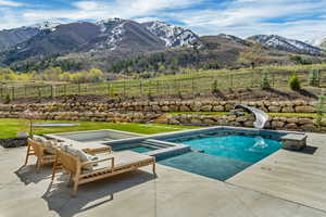View of pool with a water slide, a mountain view, a patio, and an in ground hot tub