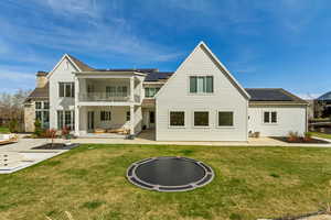 Back of house with roof mounted solar panels, a patio area, and a balcony
