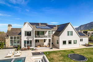 Back of property featuring a patio area, a balcony, a lawn, roof mounted solar panels, and an outdoor living space with a fire pit