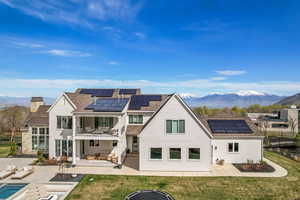 Back of house with roof mounted solar panels, a balcony, and a patio