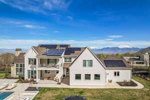 Rear view of house featuring roof mounted solar panels, a balcony, and a patio