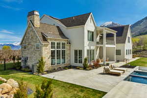 Rear view of house with a balcony, stone siding, a mountain view, fence, and a patio