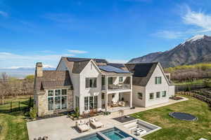 Back of house with a balcony, a chimney, an outdoor living space with a fire pit, a patio, and solar panels