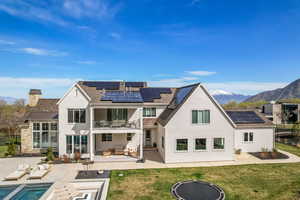 Rear view of property with an outdoor living space with a fire pit, a mountain view, solar panels, a balcony, and a patio