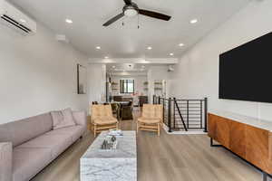 Living room featuring a ceiling fan, light wood-type flooring, an AC wall unit, and recessed lighting