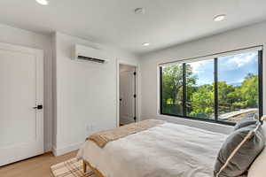 Bedroom featuring baseboards, light wood-type flooring, a wall mounted AC, and recessed lighting