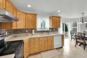 Kitchen with a notable chandelier, white dishwasher, a sink, under cabinet range hood, and electric range