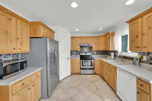 Kitchen with light tile patterned floors, light countertops, under cabinet range hood, stainless steel appliances, and a sink