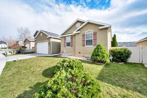 View of front of house with concrete driveway, stucco siding, fence, and a front yard