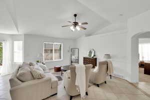 Living room featuring vaulted ceiling, light tile patterned floors, a ceiling fan, visible vents, and arched walkways