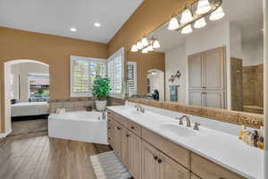 Ensuite bathroom featuring double vanity, a bath, a sink, and wood finished floors