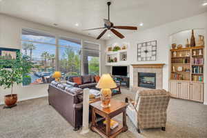 Living room featuring built in features, ceiling fan, a textured ceiling, light colored carpet, and a tiled fireplace