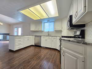 Kitchen featuring dark wood-style flooring, a peninsula, backsplash, white cabinets, and appliances with stainless steel finishes
