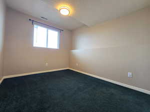 Spare room featuring baseboards, visible vents, a textured ceiling, and dark carpet