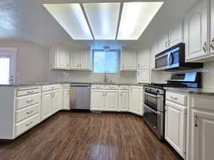 Kitchen featuring white cabinetry, appliances with stainless steel finishes, a peninsula, and dark wood finished floors