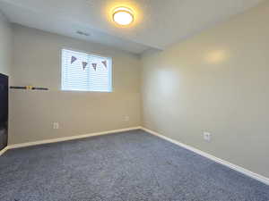 Spare room with dark colored carpet, visible vents, a textured ceiling, and baseboards